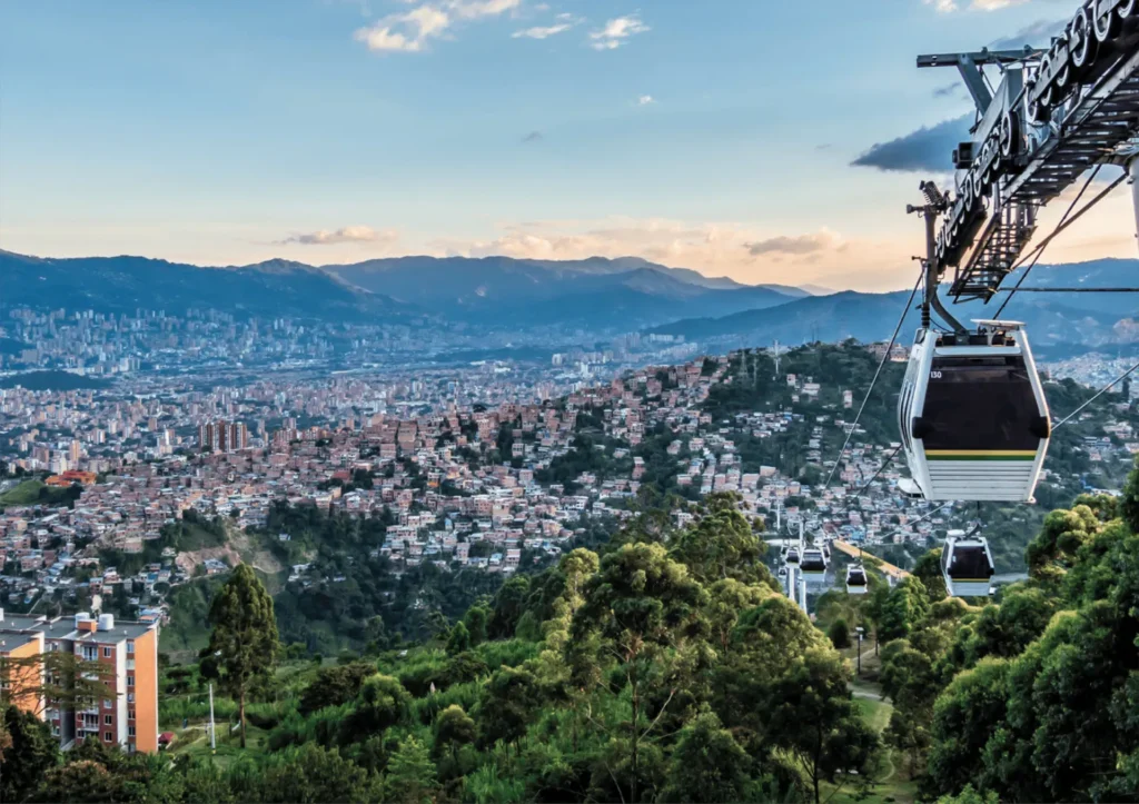 Vista panorámica de Medellín con teleféricos en primer plano y montañas al fondo.